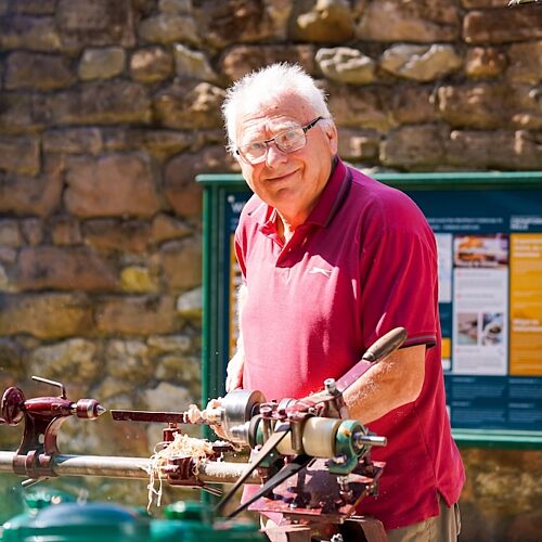 Older man wearing a red t-shirt holding machinery