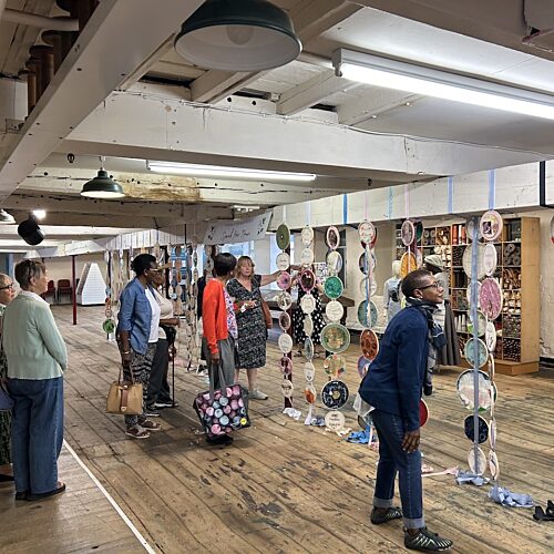 Group of women looking at an exhibition of vertical hanging individually decorated ceramic plates