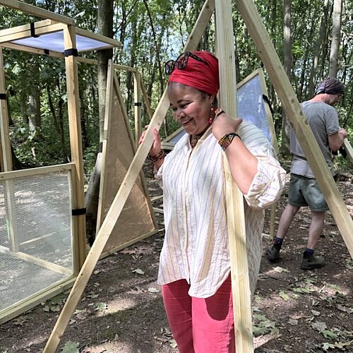 Woman carrying a wooden structure amongst trees