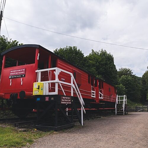 Old red railway carriage parked next to a row of stone buildings