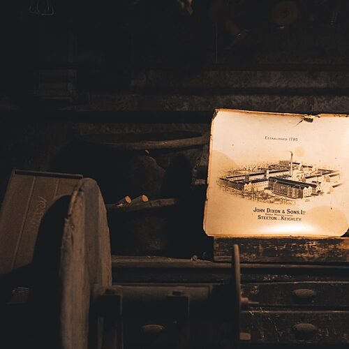 Photograph of an old illustrated image of a factory perched on an old piece of machinery