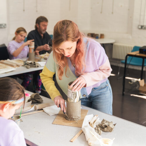 A facilitator supports a small group as they shape and build clay pieces together in a workshop setting.