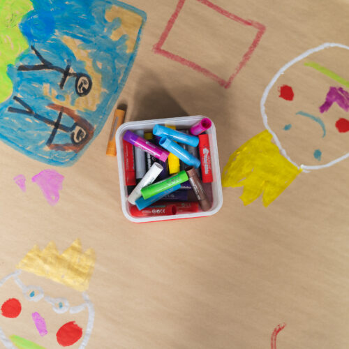 Children’s drawings and a box of colourful markers spread across paper on a tabletop.