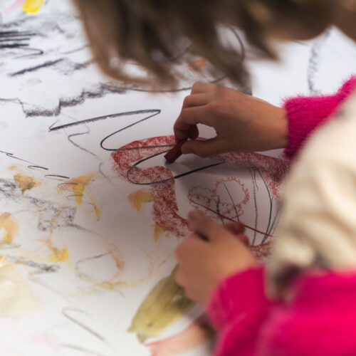 A child draws with pastels on paper, creating colourful shapes and lines.