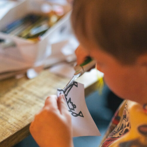 A child carefully cuts out a drawing with scissors at a craft table.