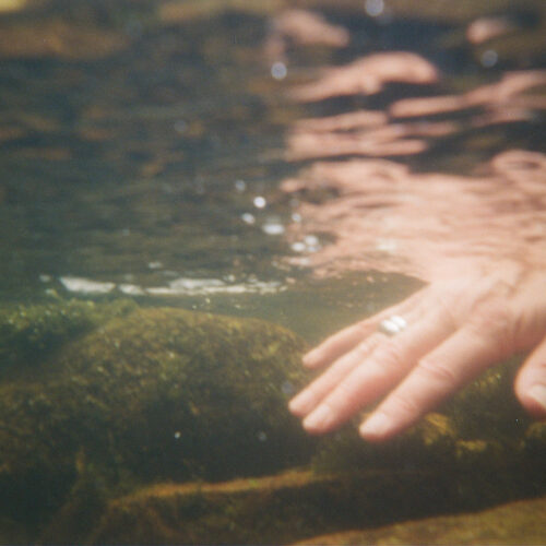 White hand wearing a silver ring seen under water on a river bed