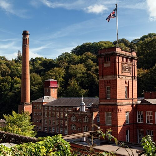 Large red-brick mill with a tower and chimney surrounded by countryside
