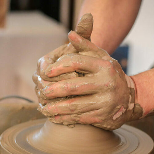 Two hands covered in clay cupping clay and shaping it on a potter's wheel