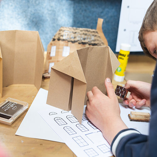 Boy making a cardboard building leans down to apply a tool to the surface