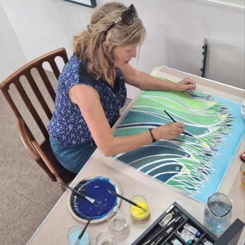 Woman wearing navy blue sat at her desk painting a watercolour in blue and green paint